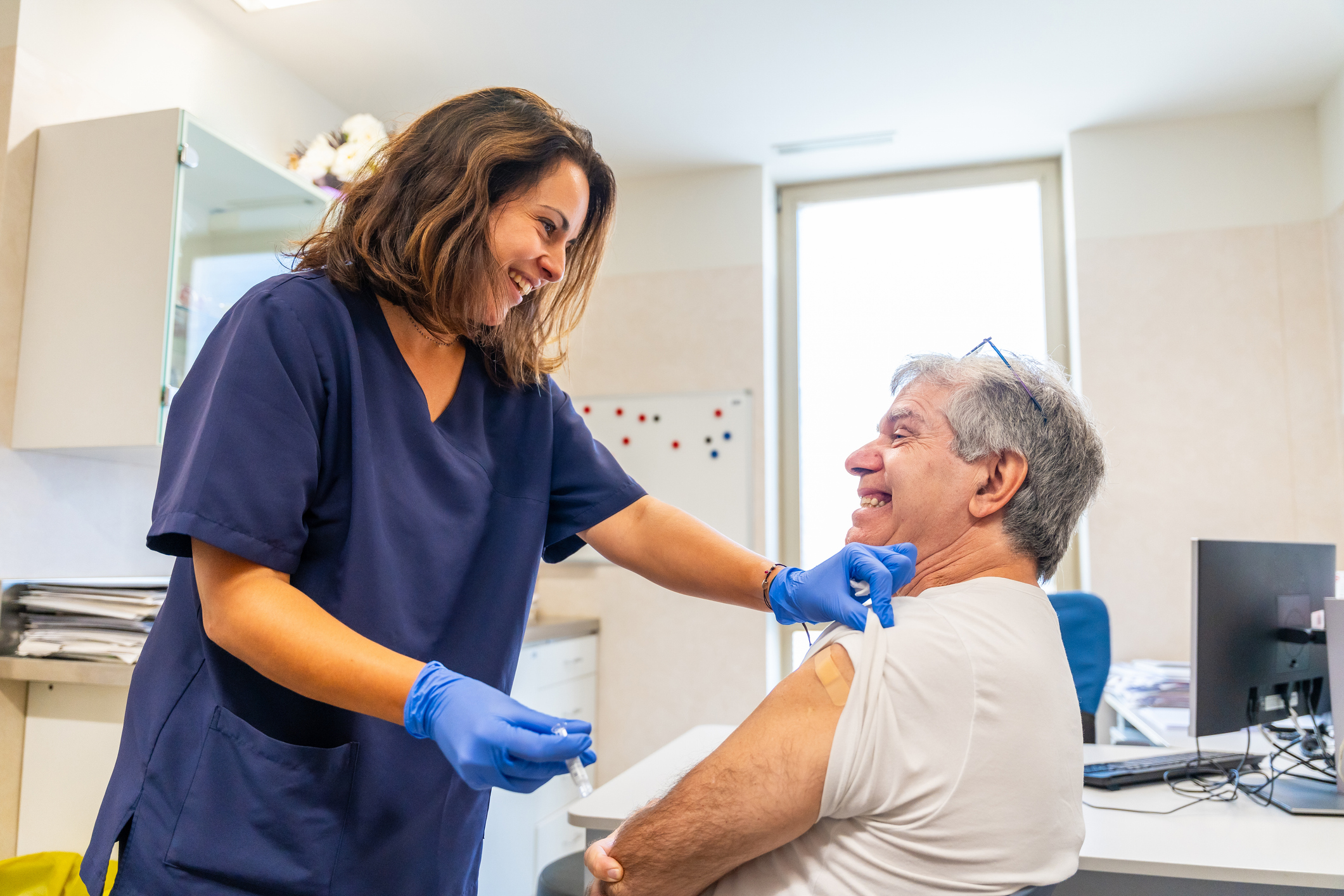 Smiling nurse giving elderly patient injection for flu vaccination campaign in a medical center to fight winter illnesses or infections