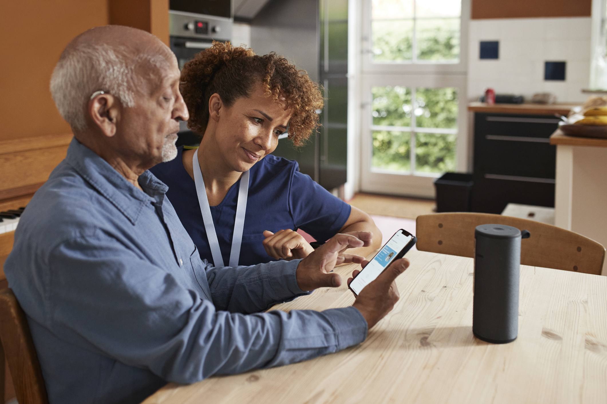 Female nurse teaching senior man to book online appointment through smart phone at table