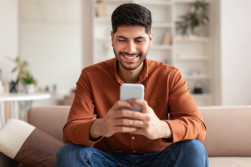 An investor smiles at something on a smartphone at home.