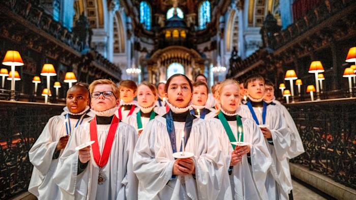 St Paul’s Cathedral choristers in white robes holding candles and singing during Christmas rehearsals inside the cathedral.