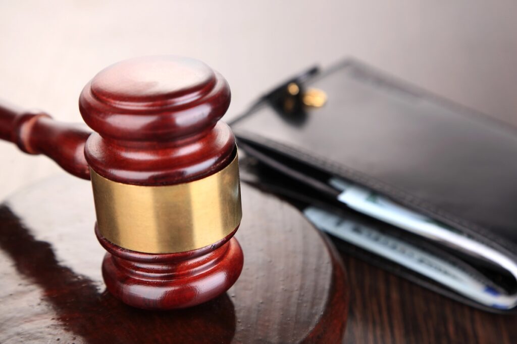 Wooden gavel resting next to a black wallet filled with cash. This symbolizes the legal resumption of wage garnishment for defaulted federal student loans starting in early 2026. Source: The College Investor