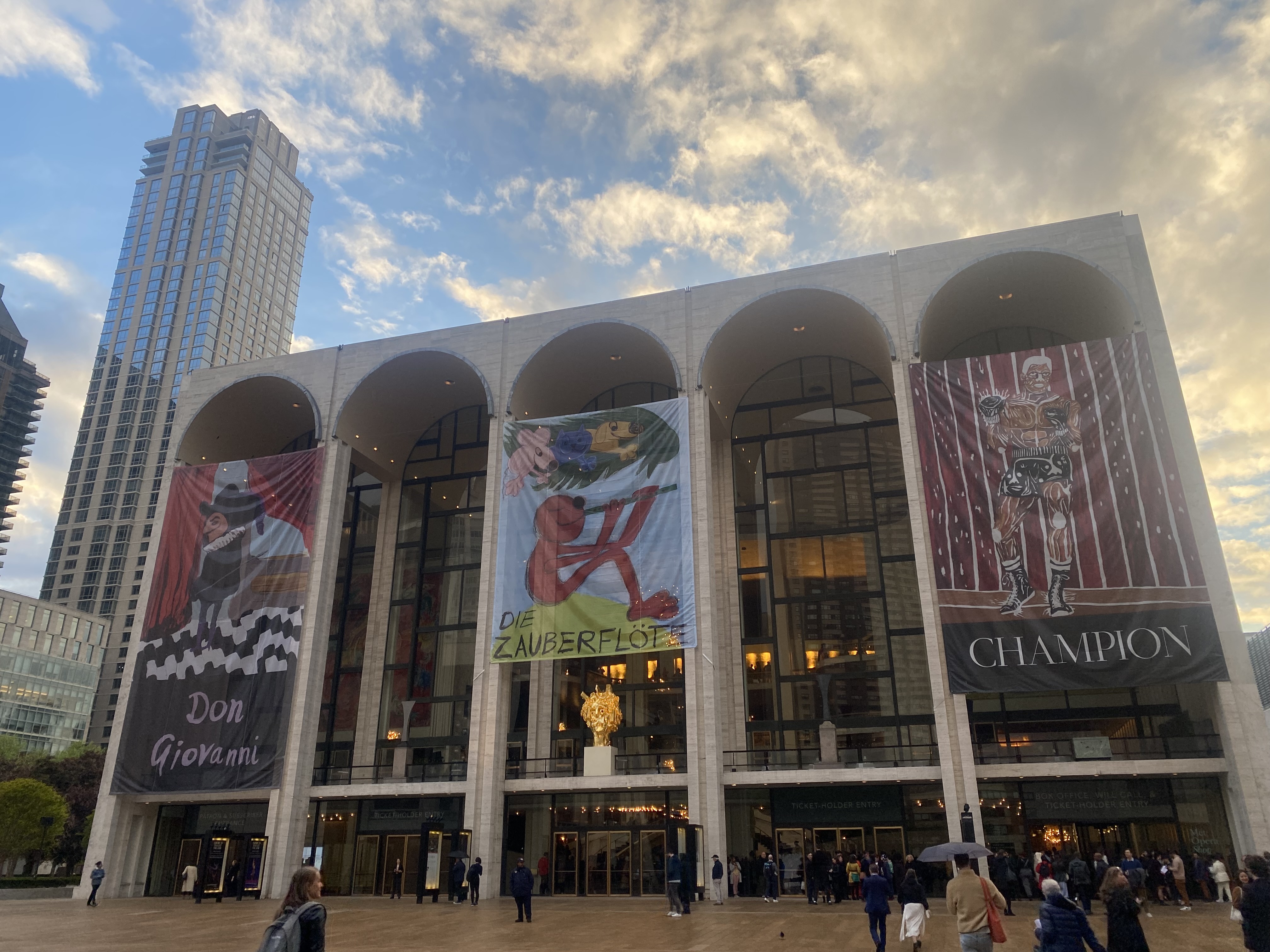 The Metropolitan Opera house seen from Lincoln Center Plaza on a clear day, with large banners for three operas.