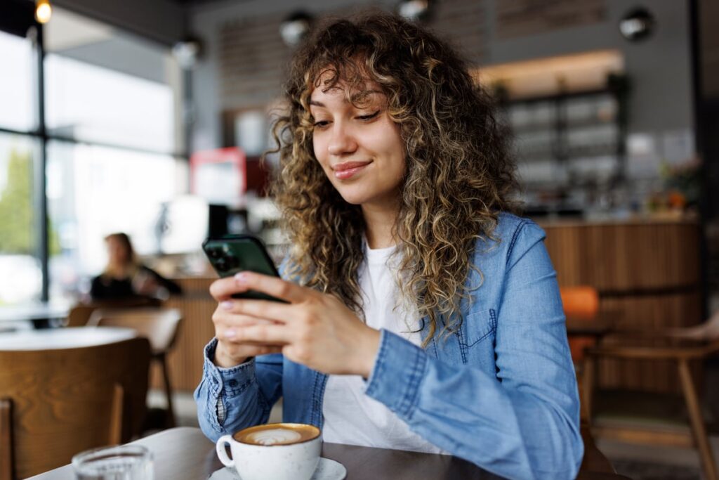 Smiling person looking at smartphone in coffee shop.