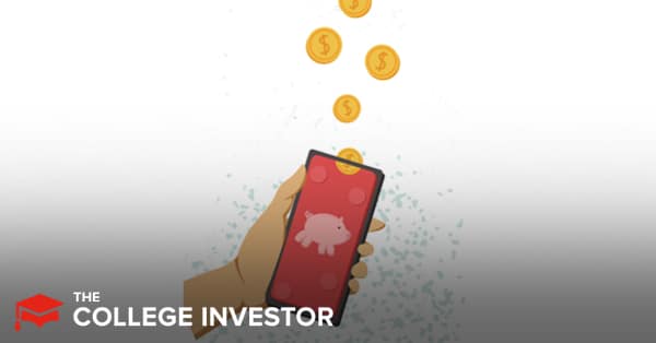 A hand, likely representing an investor, is holding a modern smartphone with a bright pink screen featuring a white piggy bank icon, symbolizing savings and investments. Above the phone, a golden coin peeking over the top edge of the phone, signifying financial growth and wealth building. The background is a minimalist white with light blue speckled accents, suggesting a clean and user-friendly experience. This image visually encapsulates the article's focus on the top automatic investment apps for 2026, emphasizing how these "set it and forget it" platforms simplify investing and help individuals build wealth through disciplined savings, making them ideal for buy-and-hold investors.