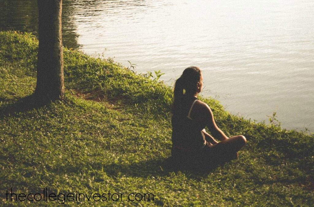 A woman doing yoga in a park by a lake, representing the free hobbies that you can do. Source: The College Investor