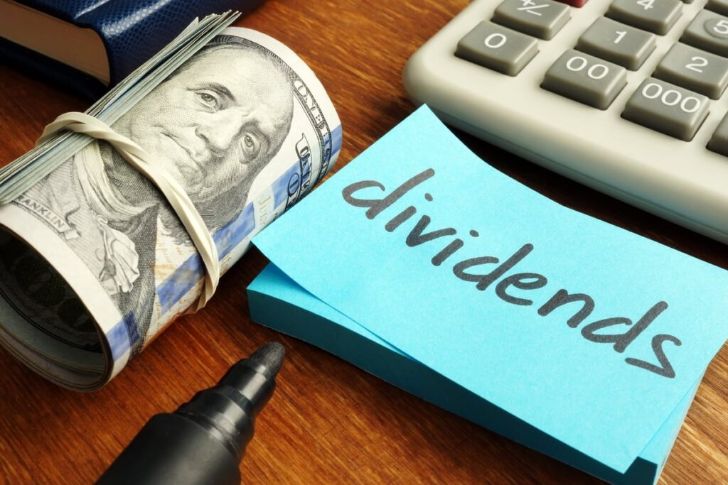 A roll of cash next to a sticky note with the word, dividends, written on it.