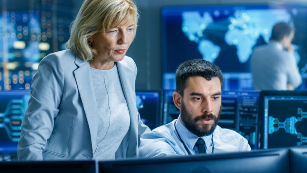 Two people in an office, looking at a computer monitor and discussing what is on it.