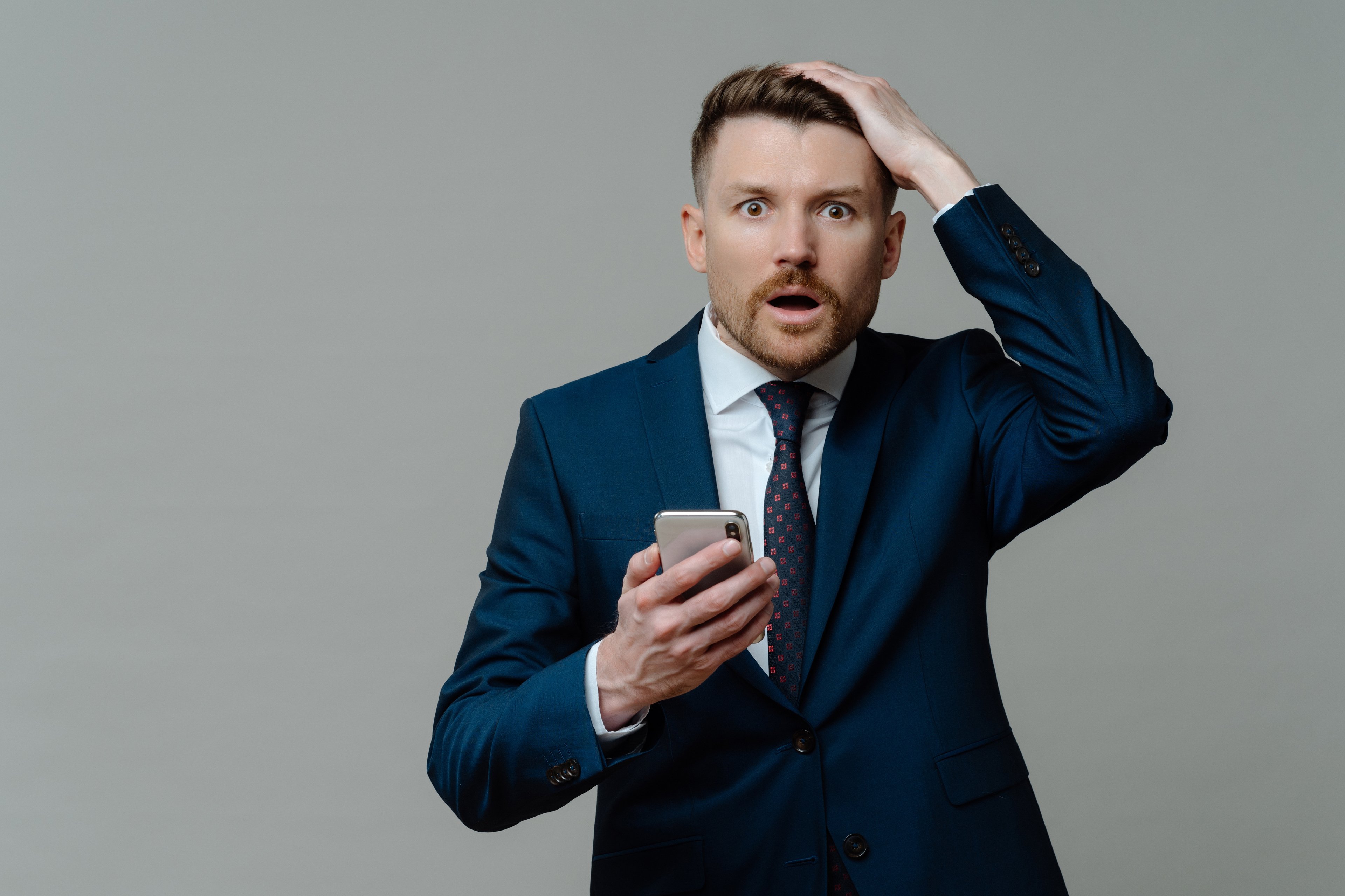 Shocked person in suit, holding a smartphone.
