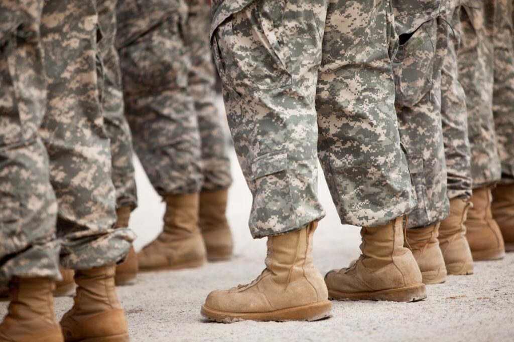 Soldiers stand in a row, shown from their knees down.
