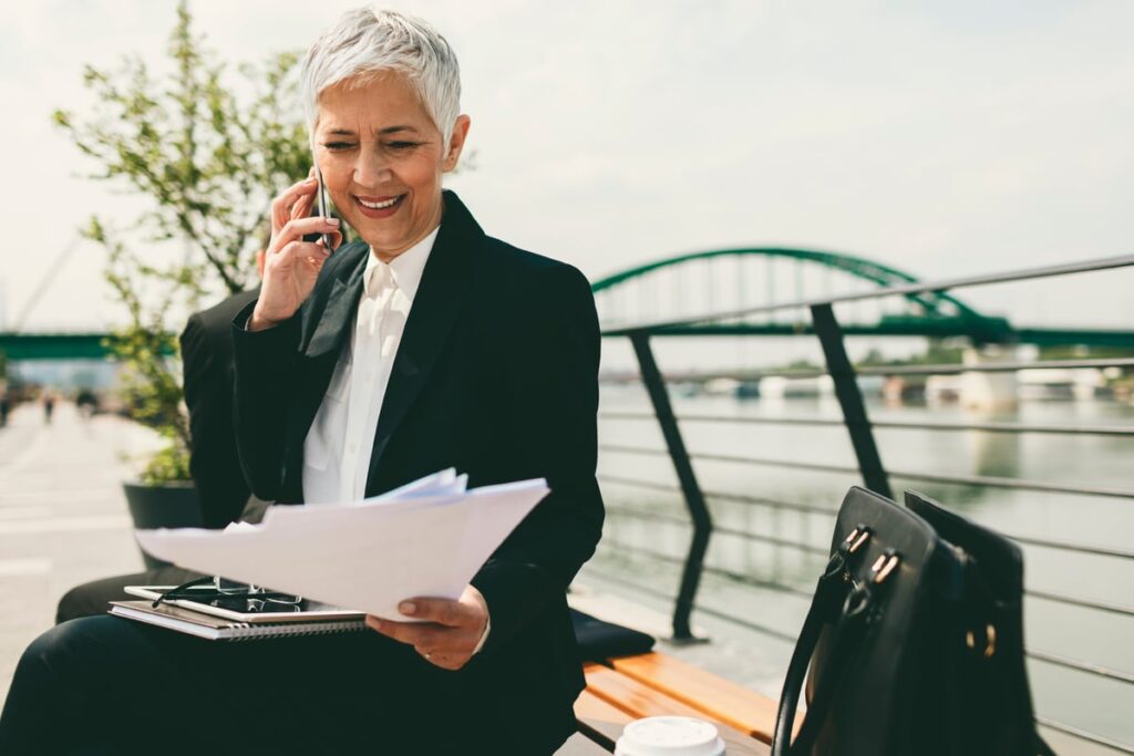 A smiling businessperson talking on a phone on a bench outside.