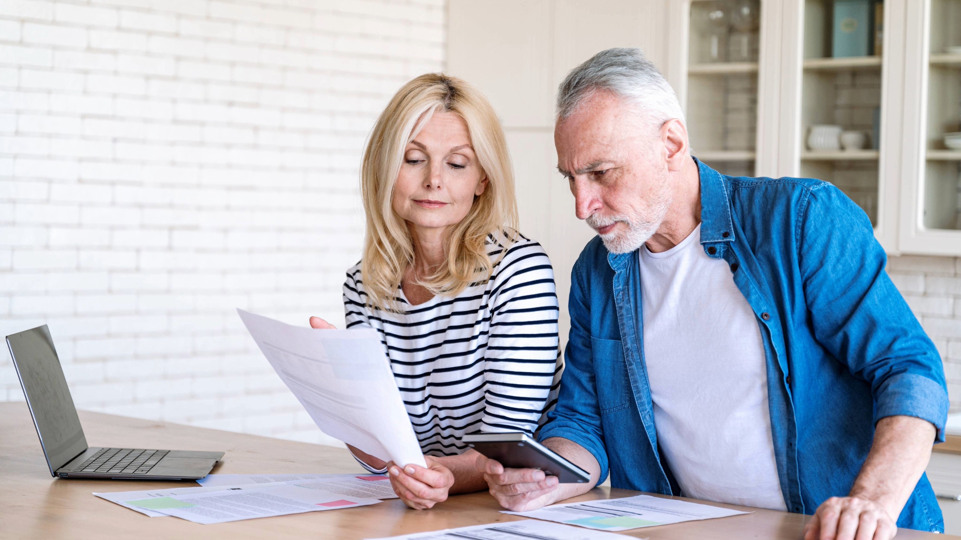 Worried mature man and woman check finance account in kitchen