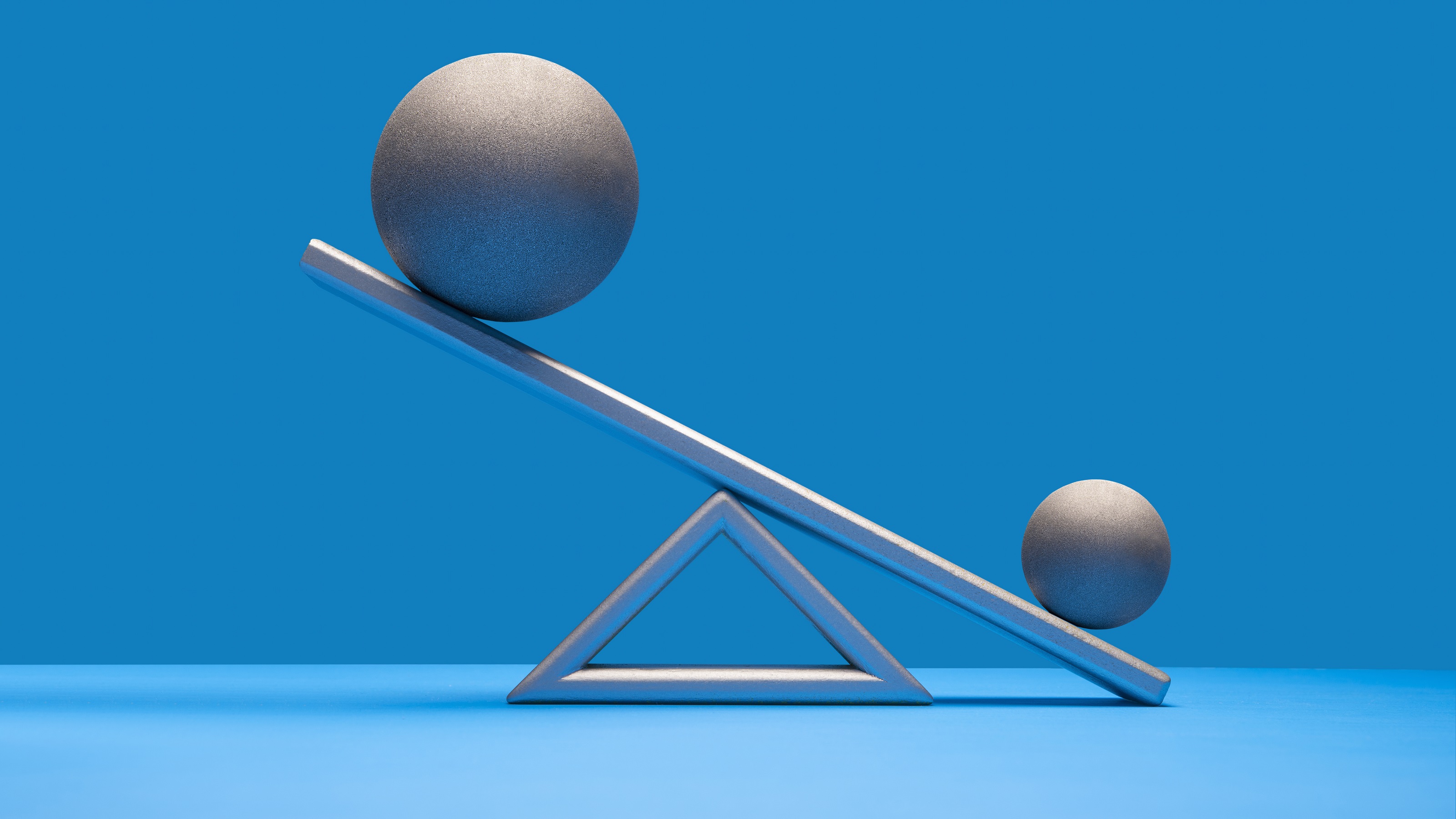 A larger ball is up in the air on a scale, while the smaller ball is down.