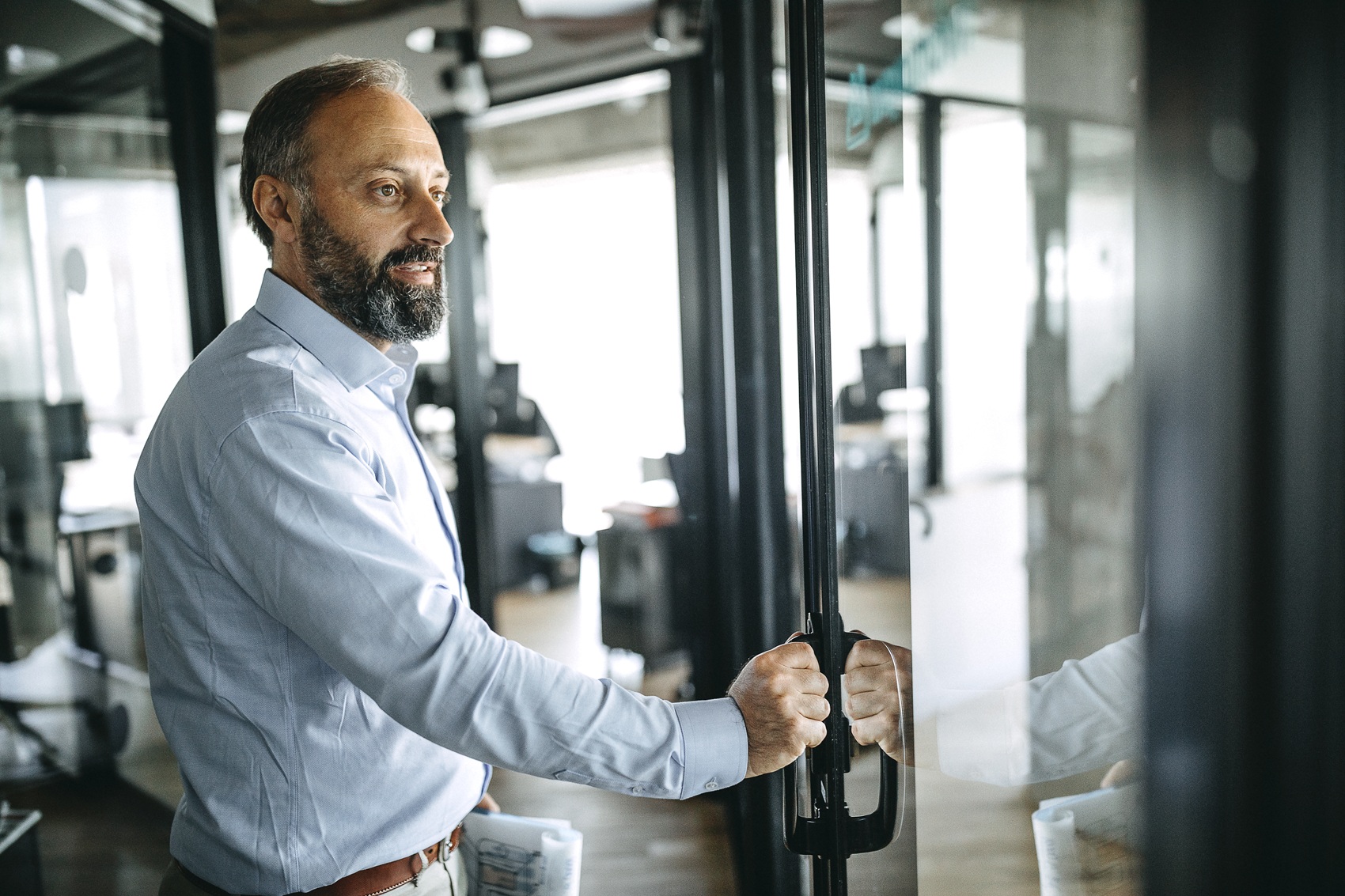 Side view of a businessman holding financial report at doorway opening door in office