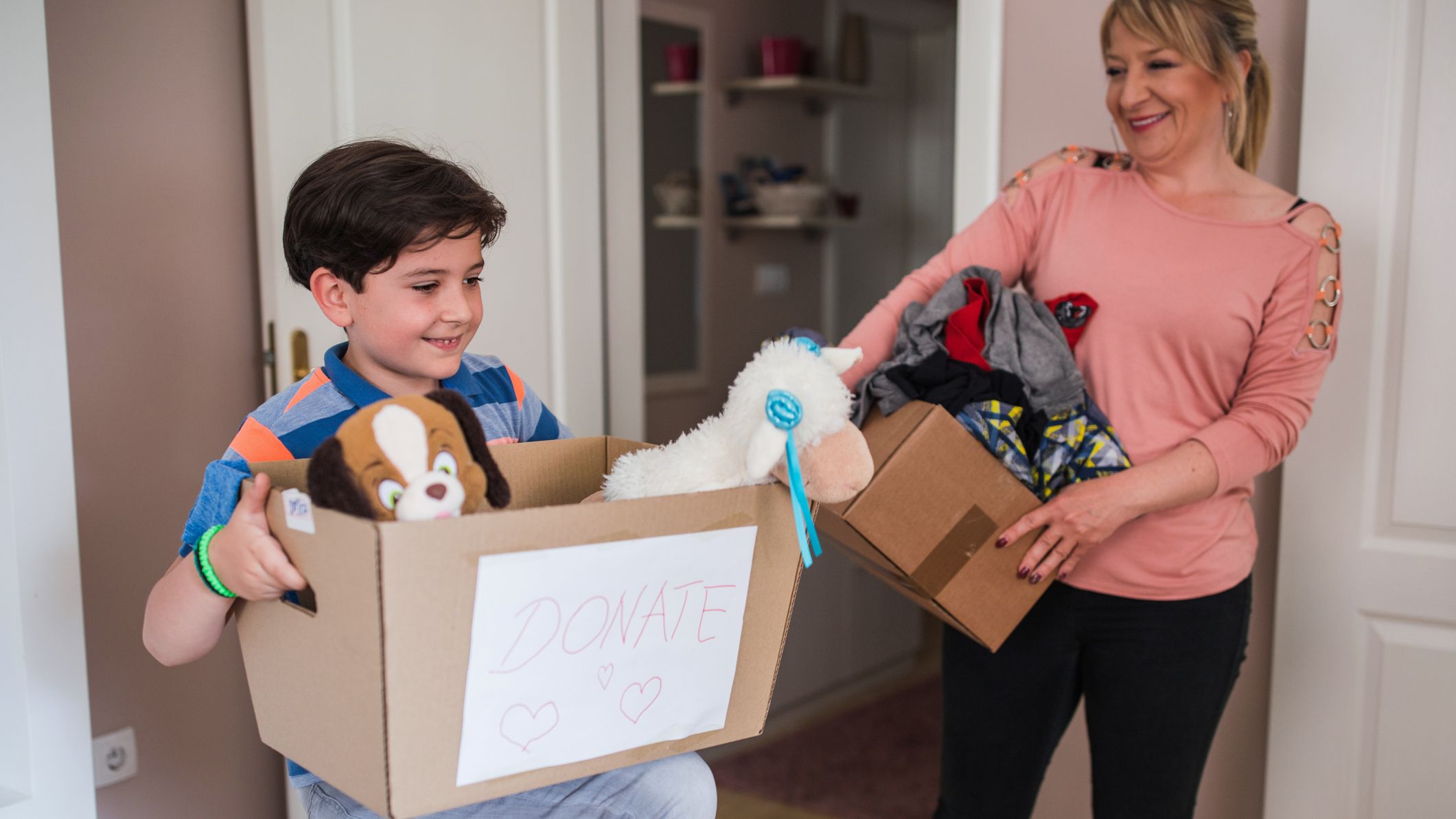 Happy woman and her son both holding boxes full of stuff for donation