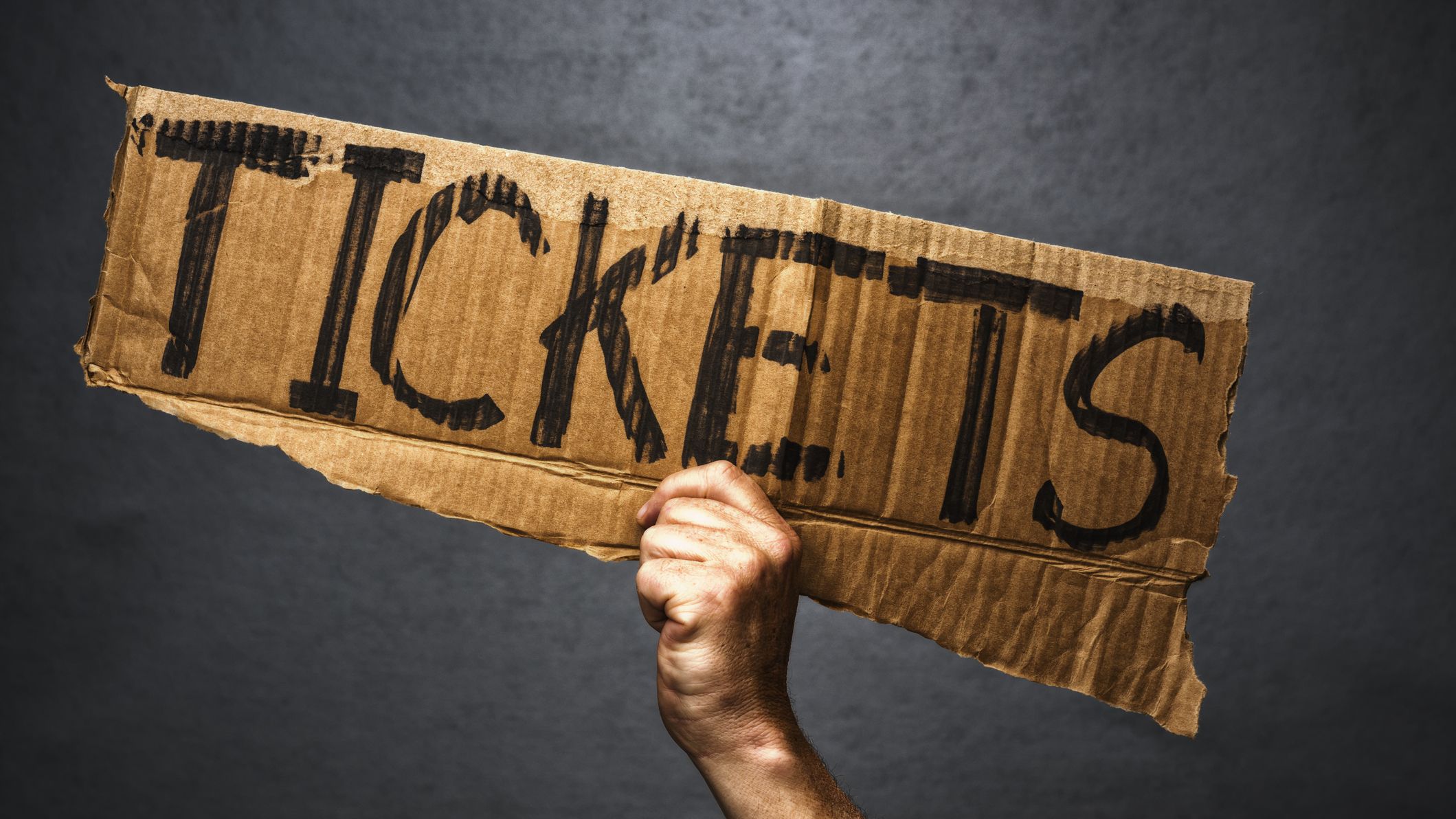 Hand holding cardboard sign with Tickets written on it