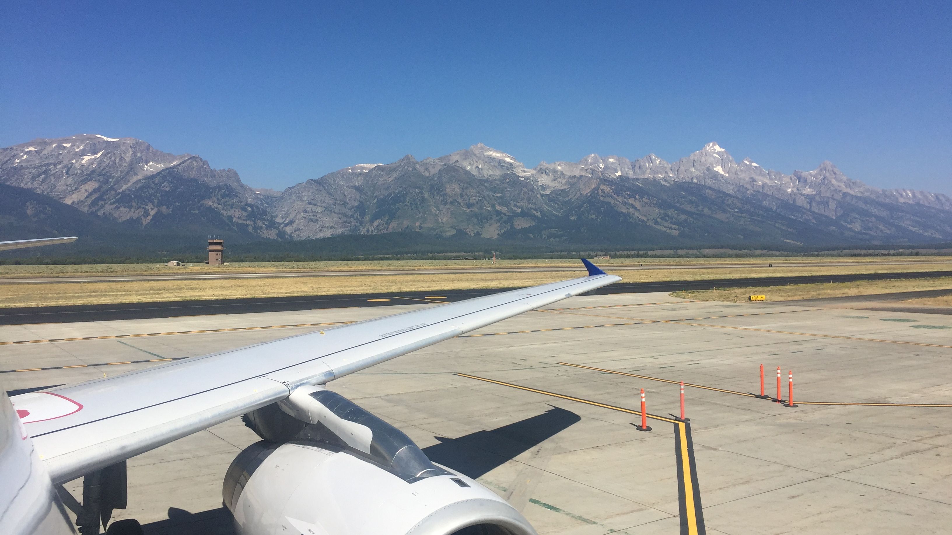 The wing of a plane on a runway at Jackson Hole Airport, with mountains in the background.