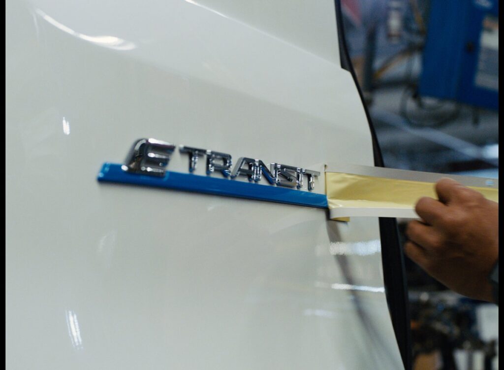 Person peeling tape off the logo on a Ford E Transit vehicle.