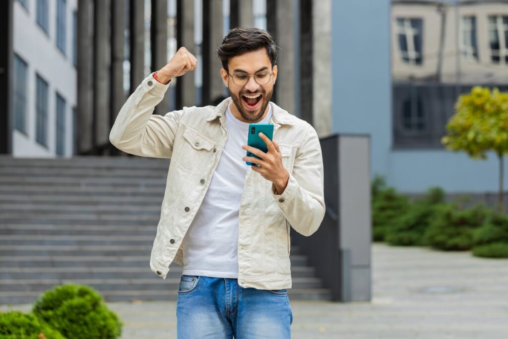 Investor with a smartphone is celebrating with a fist pump.