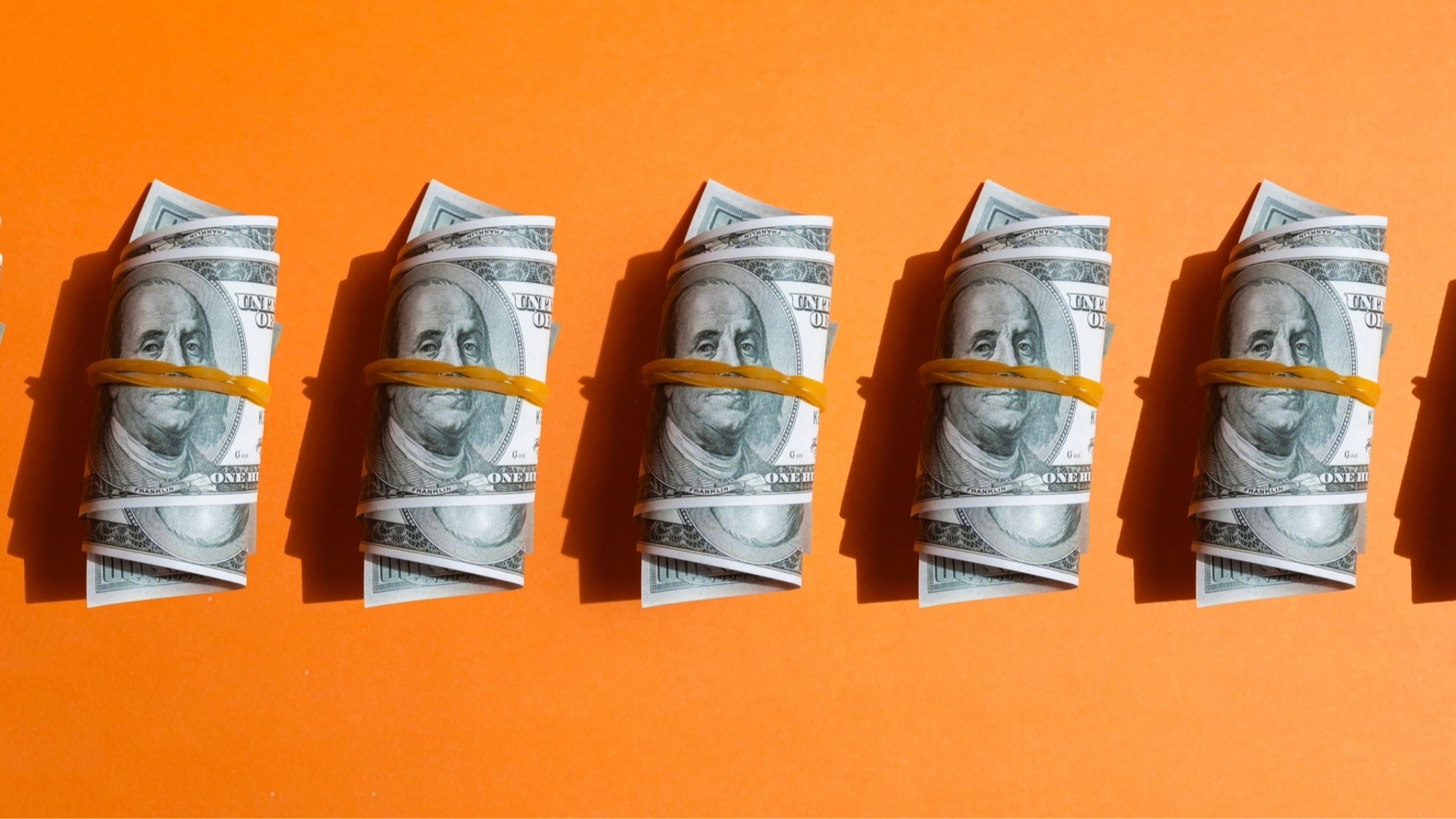 5 bundles of one hundred dollar bills wrapped in elastic bands on orange background