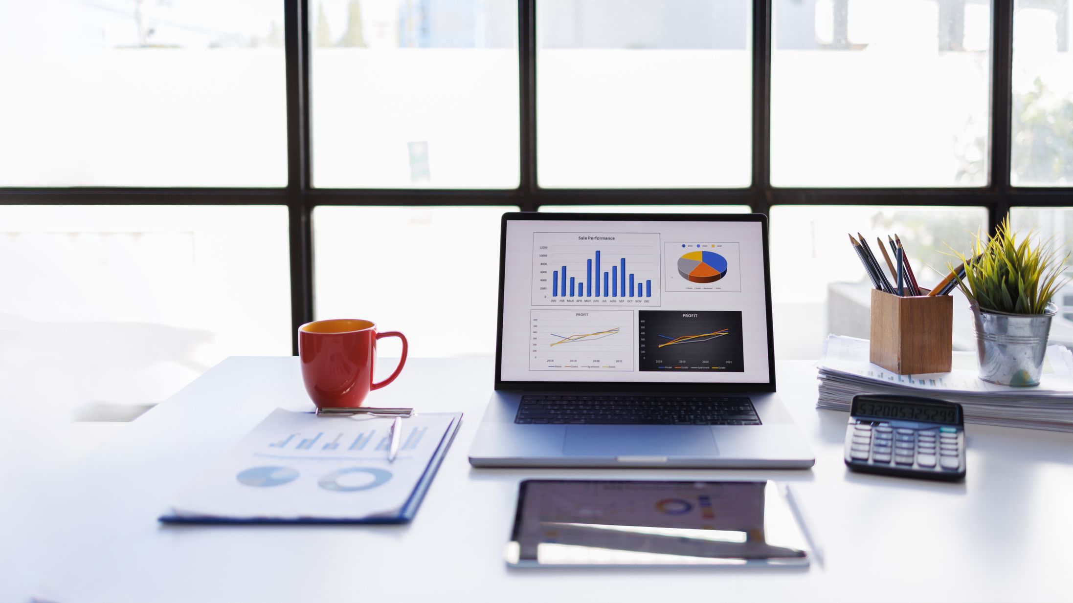 a desk with a coffee cup, financial projections and an open laptop with bar graphs and pie charts