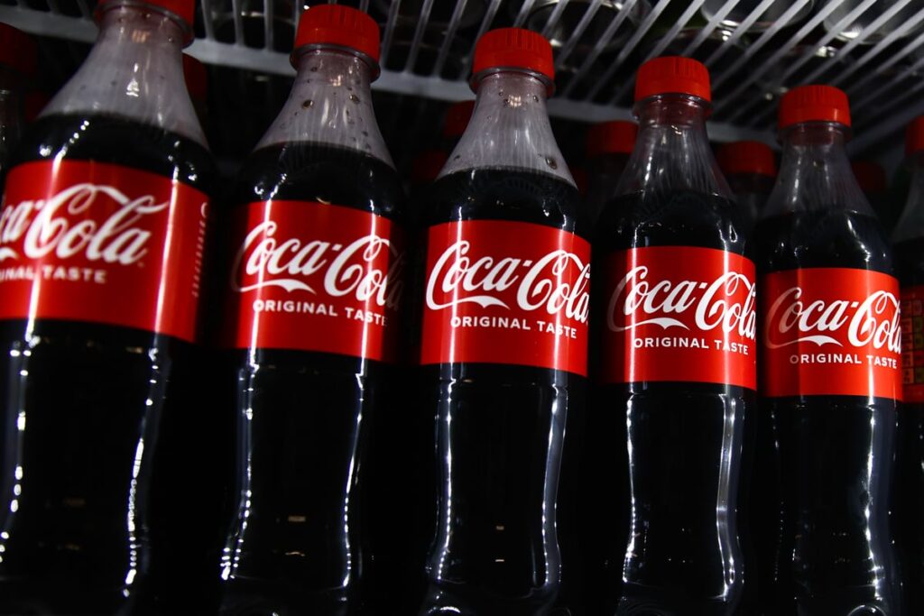 Row of Coca-Cola bottles lined up in fridge.