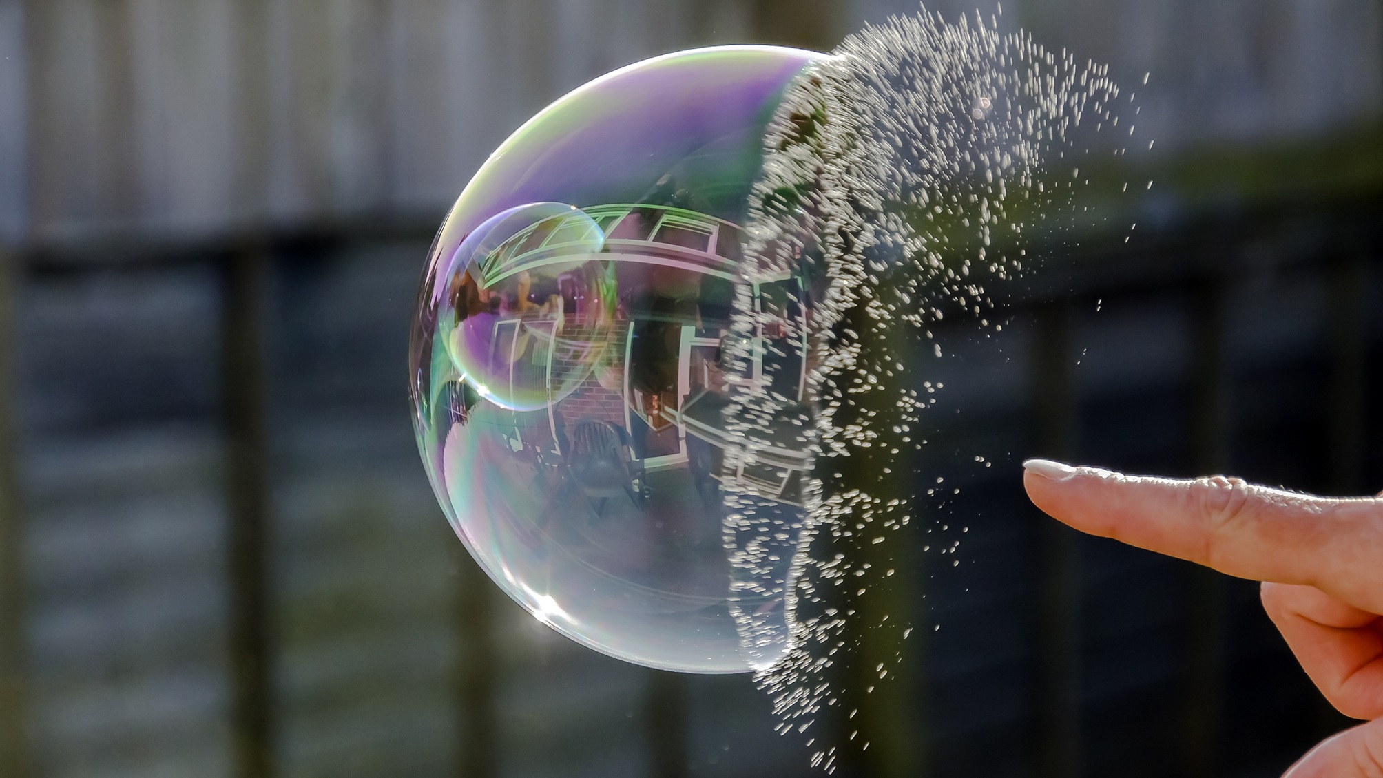 A finger pokes a bubble, and it's captured in mid-burst.