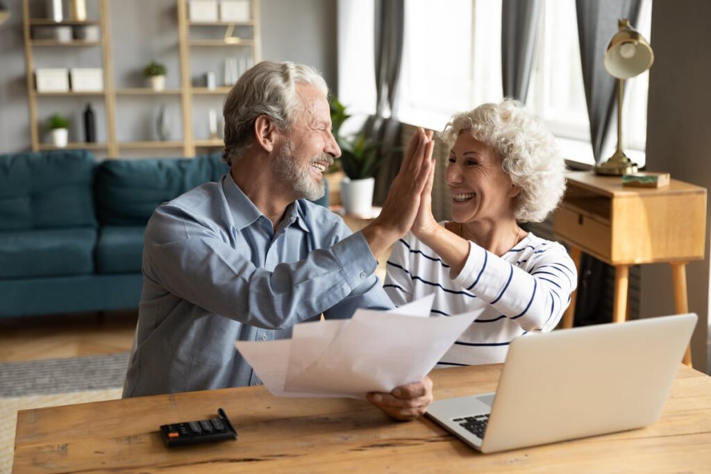 Two smiling people sit in front of a laptop, high-fiving each other.