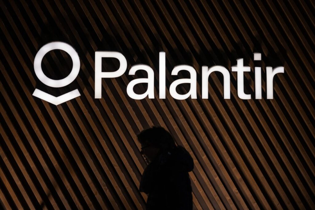 The Palantir logo on a wall with a silhouette of a person underneath it.