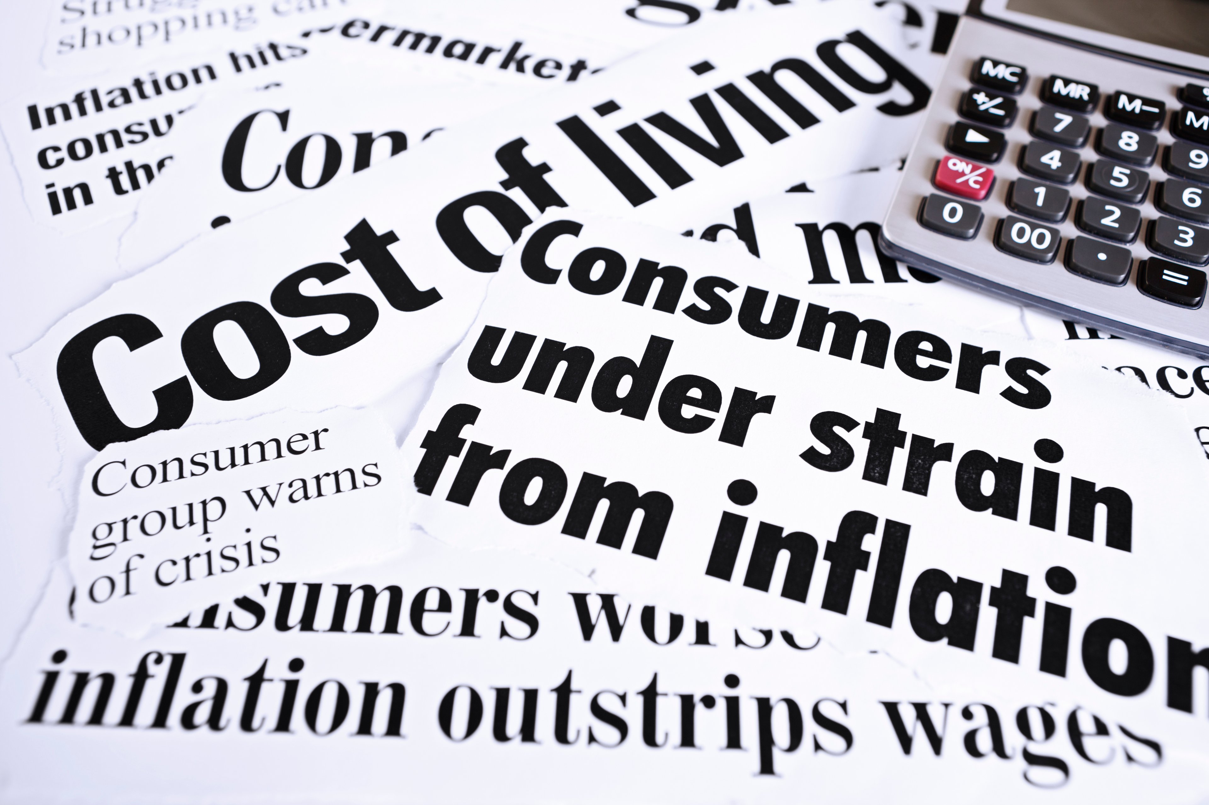 A calculator placed next to several newspaper clippings highlighting rising prices. 
