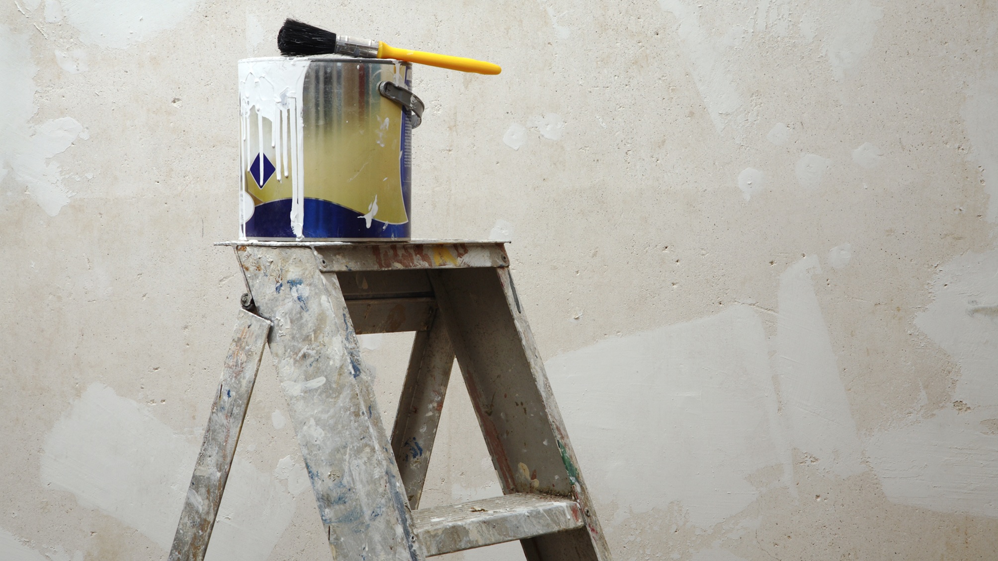 A ladder with a paint can and paintbrush on top.