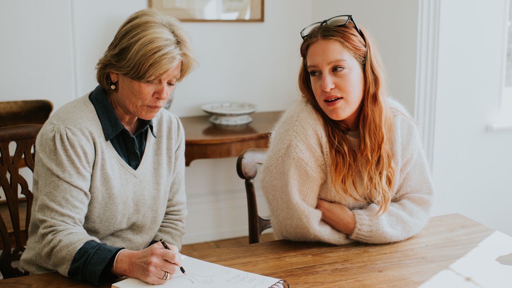A senior woman taking notes will sitting with her children at a dining table.