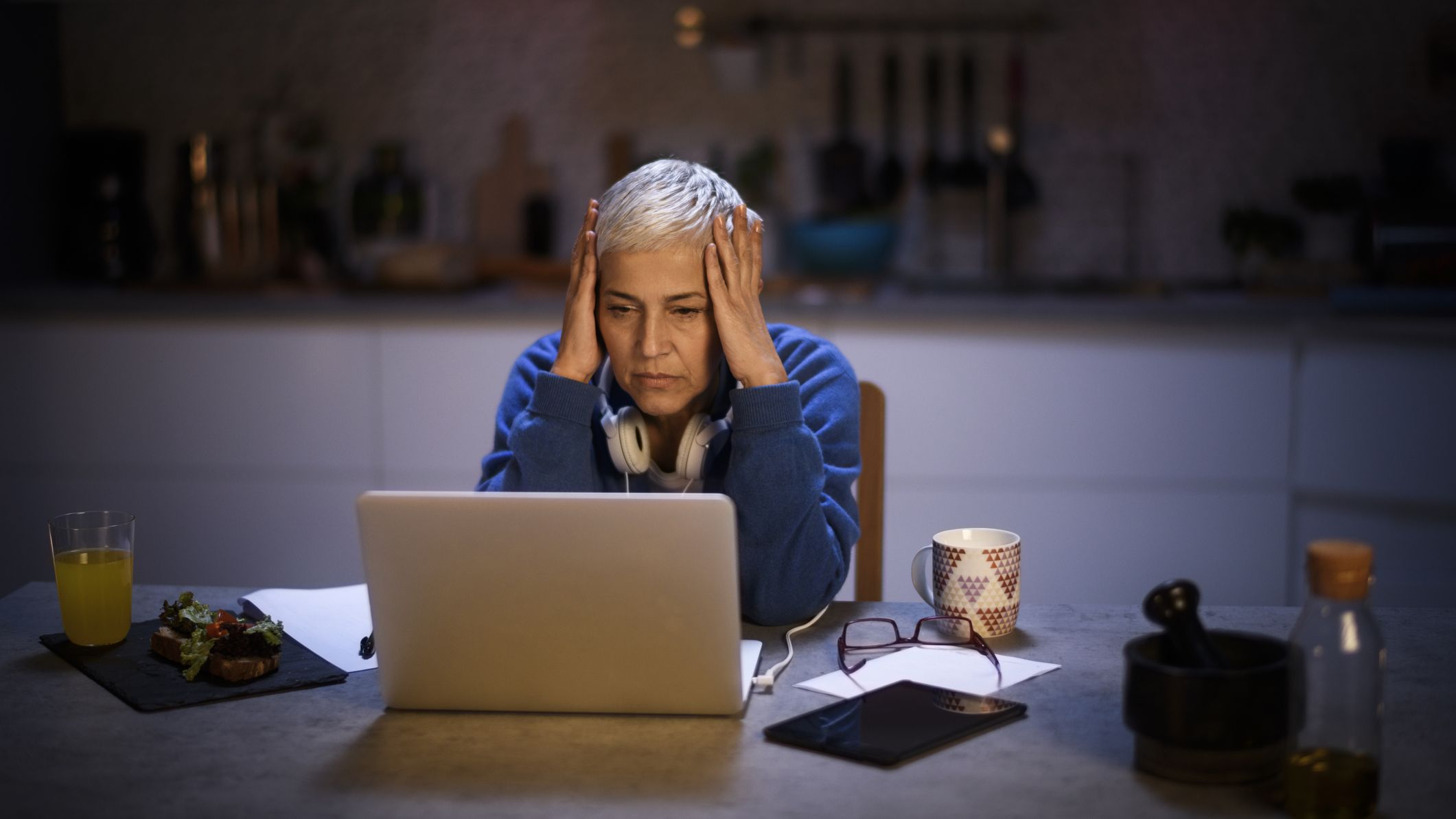 A senior woman in a dark kitchen looking stressed about her finances.