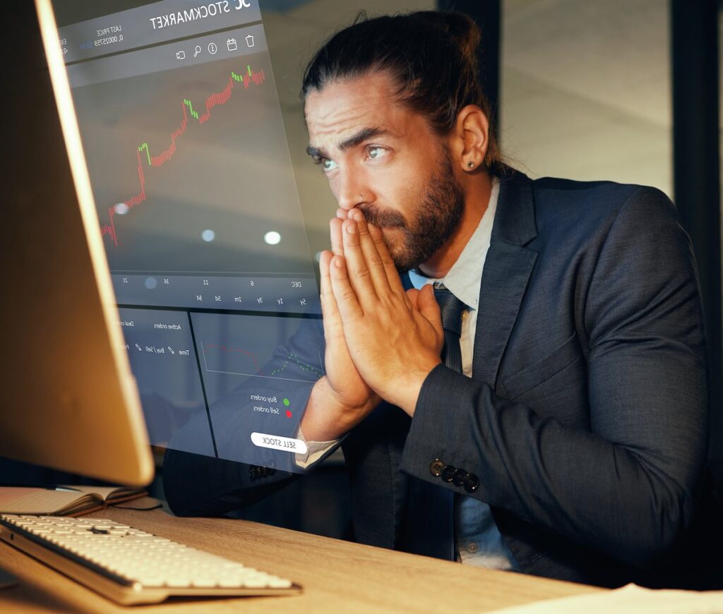 Worried-looking person looking at downward-trending stock chart on computer.
