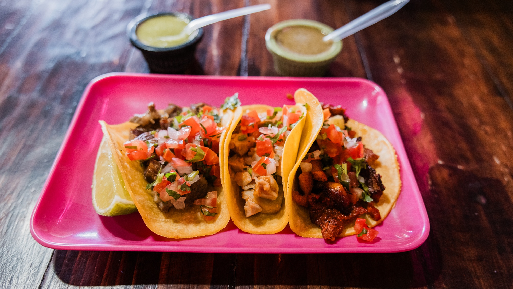 Three street tacos an a square pink plate at a restaurant.