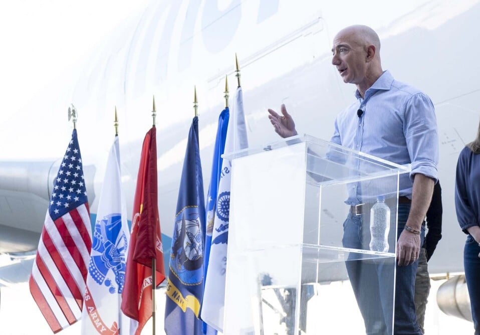 Jeff Bezos making a speech next to a bunch of flags.