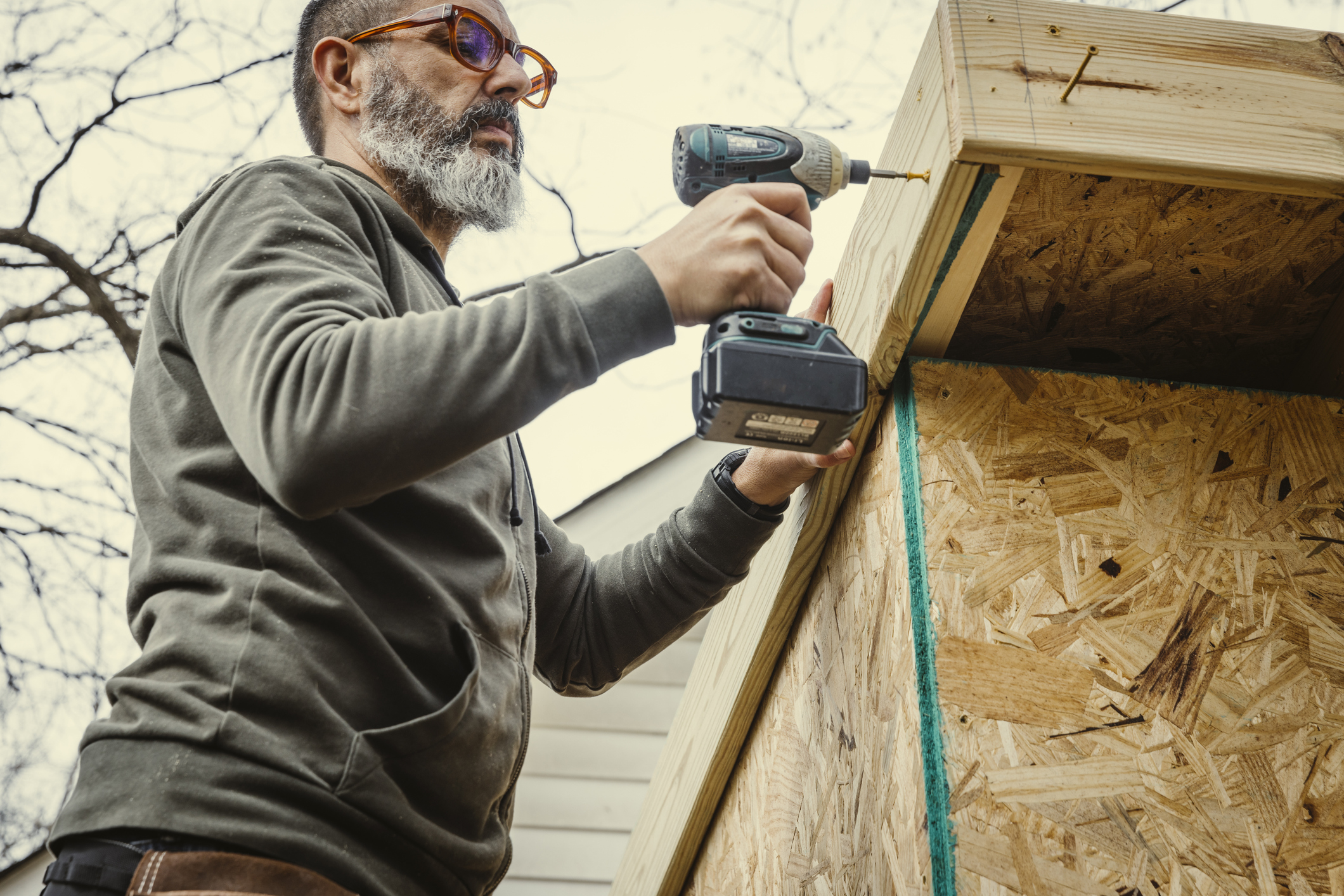Older man working on his home with a power tool.