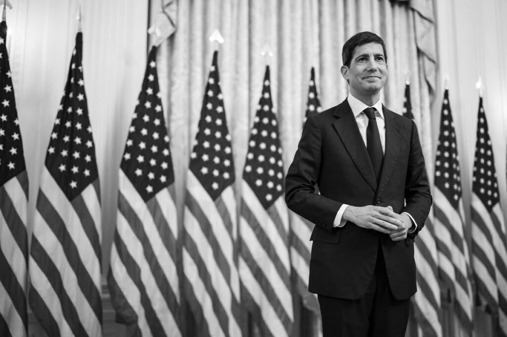 Fed Reserve Chairman Kevin Warsh standing in front of a row of American flags.