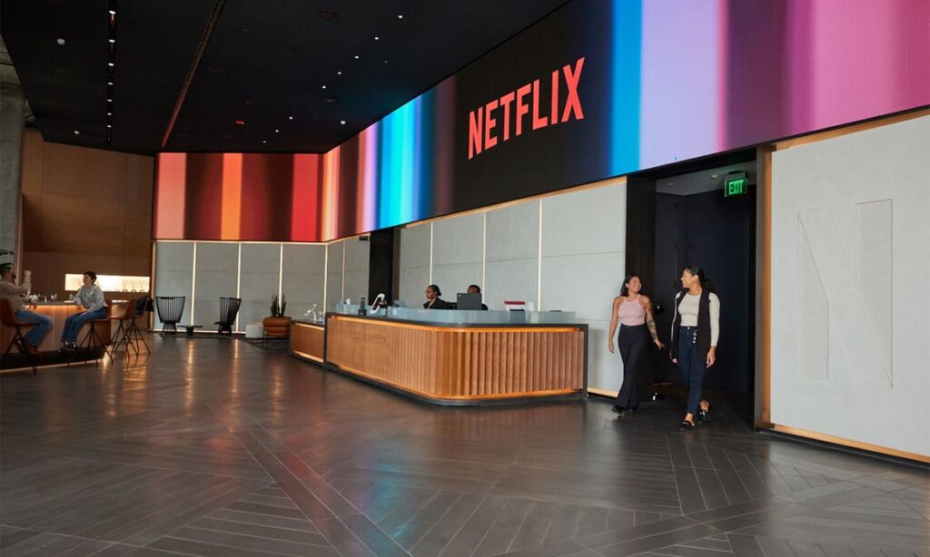 Netflix office lobby with a reception desk, colorful wall display, and employees walking and seated.