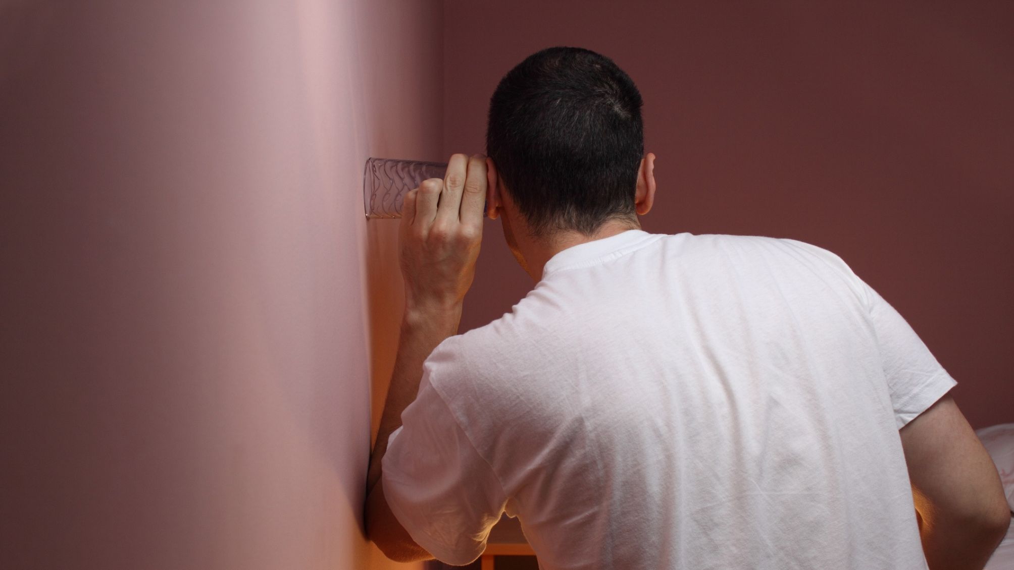 Man eavesdropping through a bedroom wall using a glass