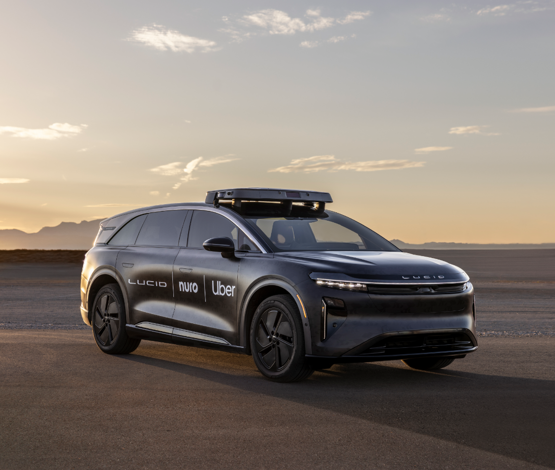 A black Lucid robotaxi with Lucid, Nuro, and Uber logos on it, at dawn or dusk.
