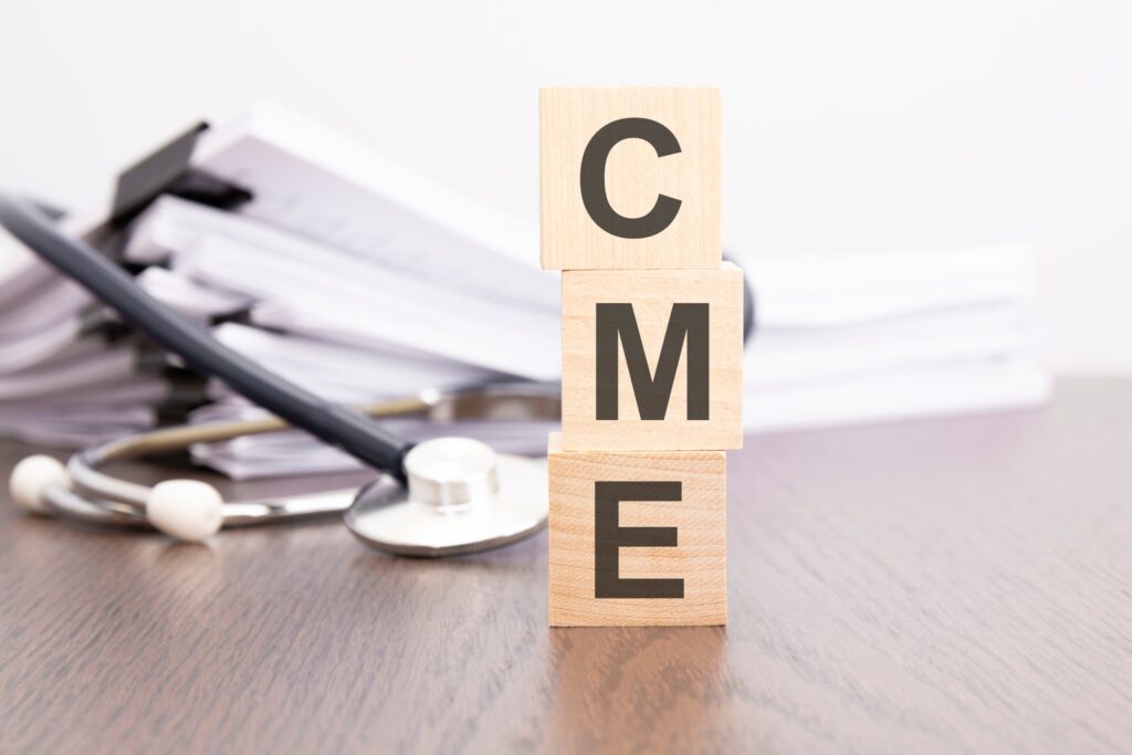 text CME is written on wooden cube near a stethoscope on a dark background.
