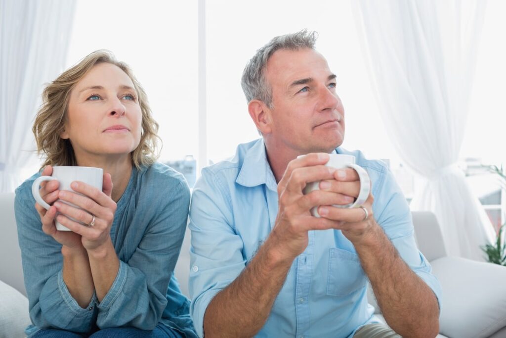 An older couple drinking coffee and looking off in the distance.