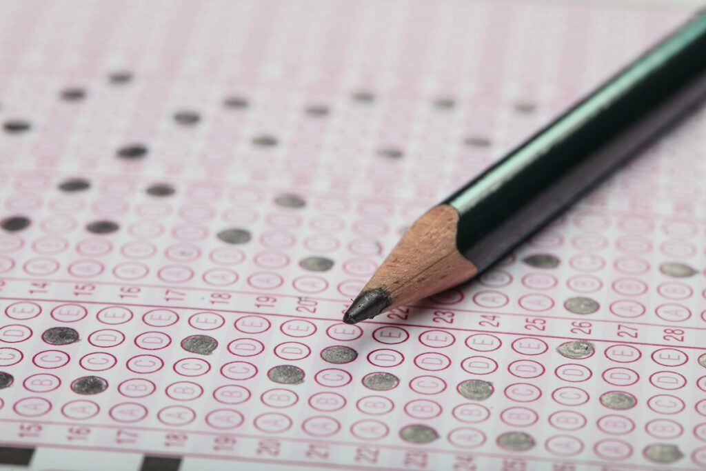 School Students hands taking SAT exam, writing examination holding pencil on optical form of standardized test with answers sheet doing final exam in classroom.