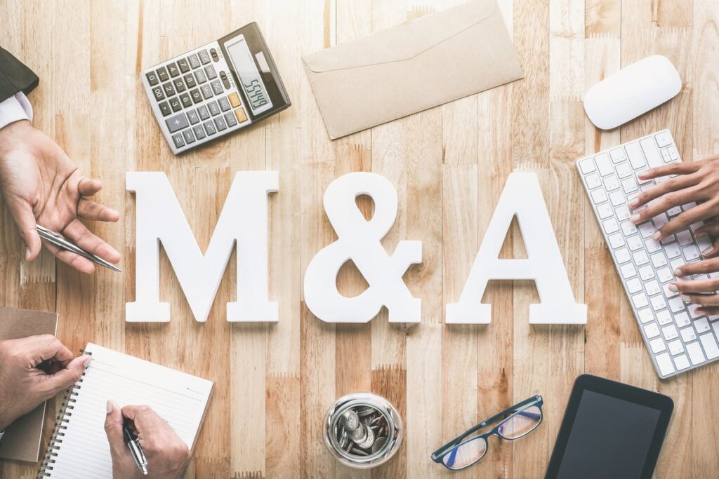 The letters M and A, indicating mergers and acquisitions, on a table with hands around it depicting negotiations.